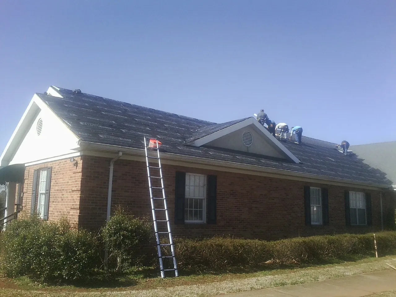 Crew tearing shingles off a brick ranch roof with a ladder set — Metal Roof Repair work by our crew in Micaville
