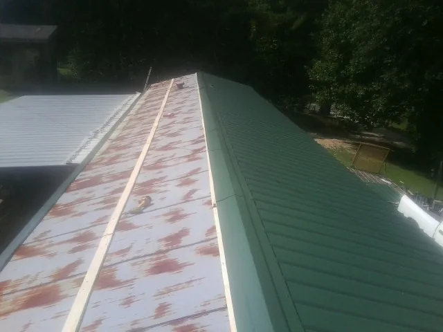 Old rusted panels beside newly installed green metal roofing — Wind Damage Roof Repair by Roofing Brothers in Micaville