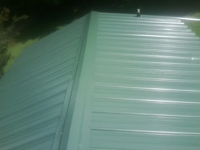 New green metal panels meeting at the ridge of a roof — Flat Roof Repair work by our crew in Micaville