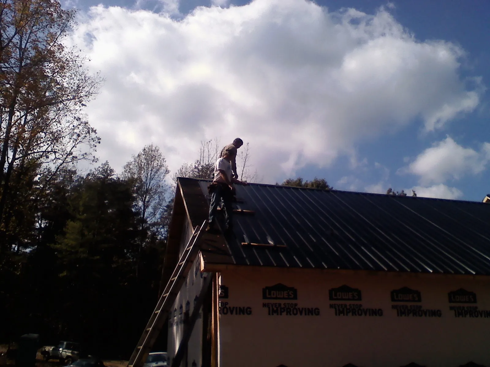 Roofer fastening dark metal panels high against a cloudy sky, from a Roof Inspection job in Micaville