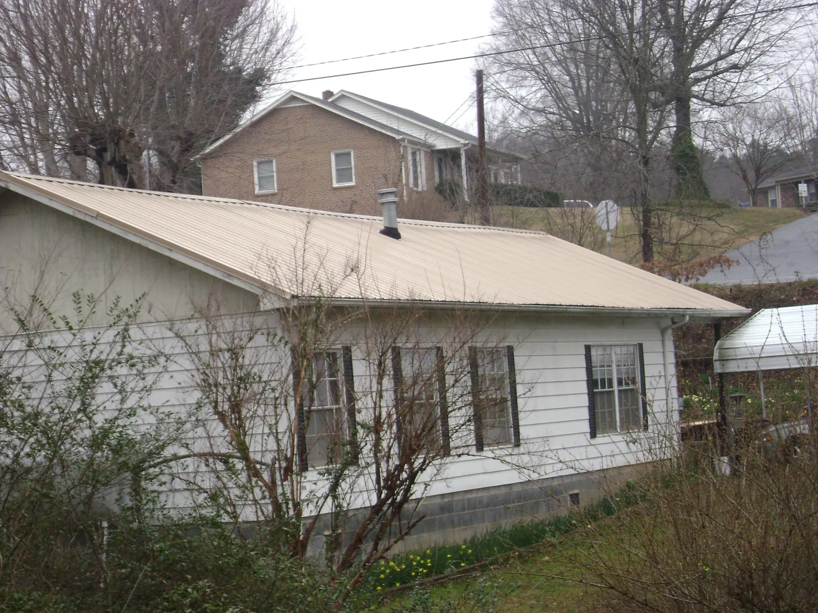 Tan metal roof on a white sided house set into a hillside — Commercial Roofing by Roofing Brothers in Micaville