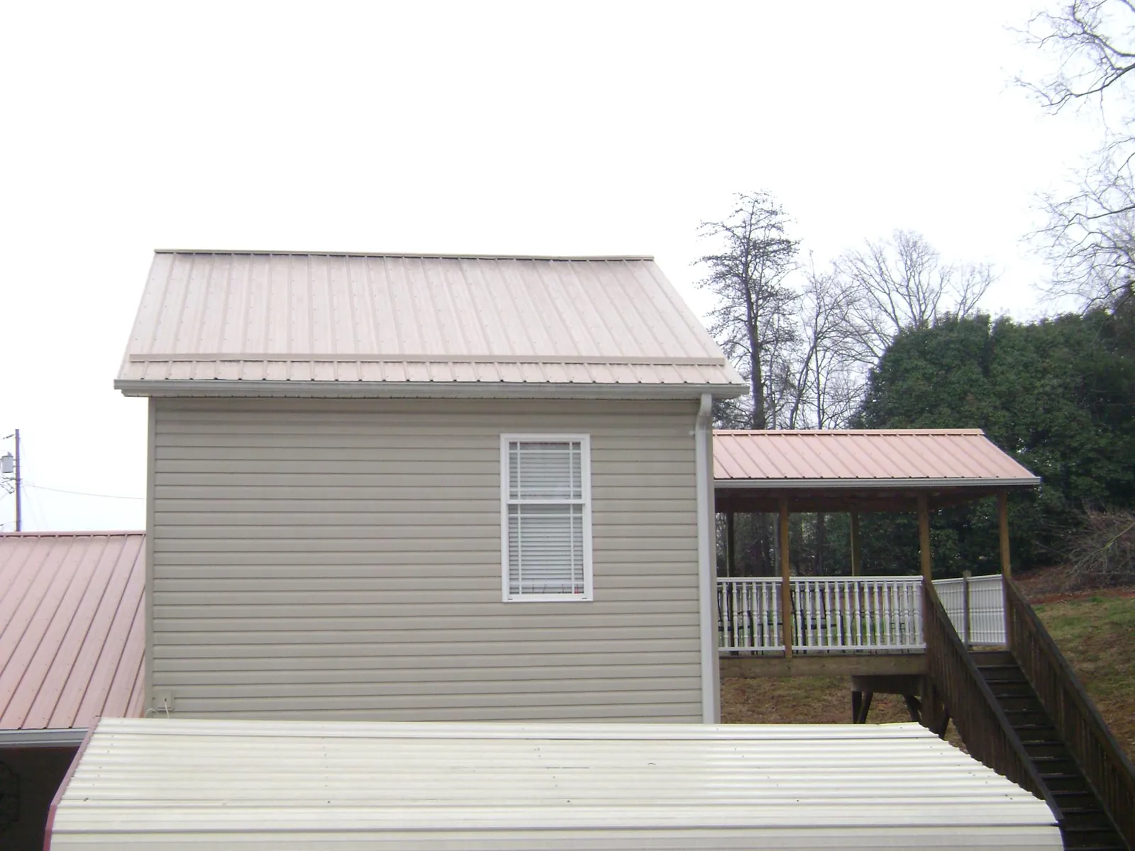 Tan metal roofs on a two story addition and attached porch, from a Roof Replacement job in Micaville